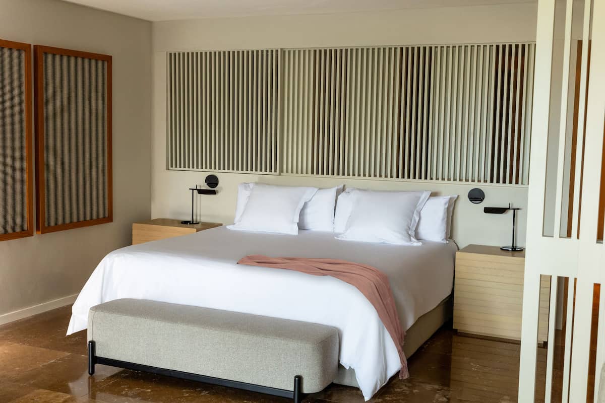 Quarto moderno com uma cama grande, mesas de cabeceira, um banquinho e cabeceira ripa.