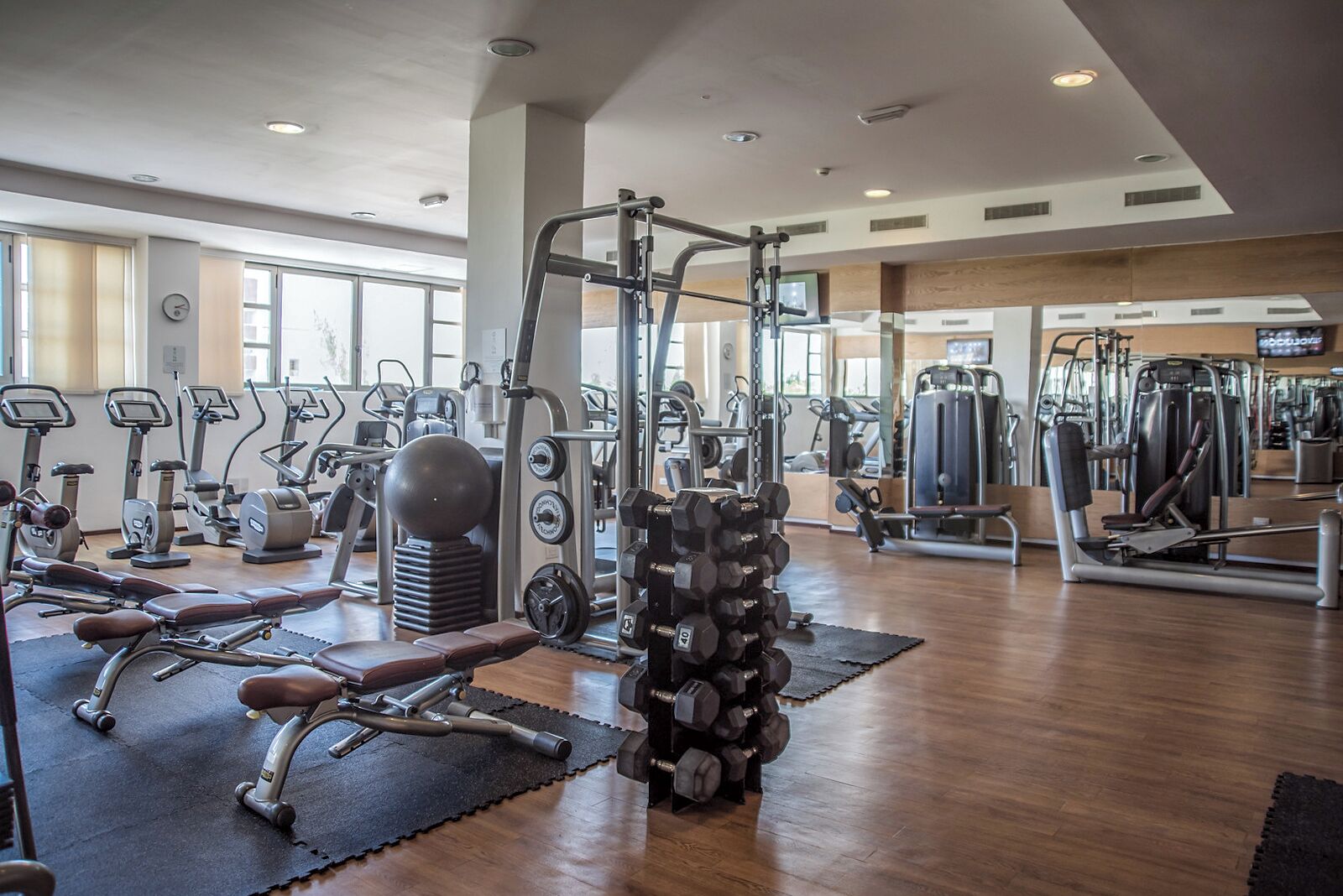 Un gimnasio con diversos equipos de ejercicio, incluyendo cintas de correr, máquinas de pesas y pesas sueltas.
