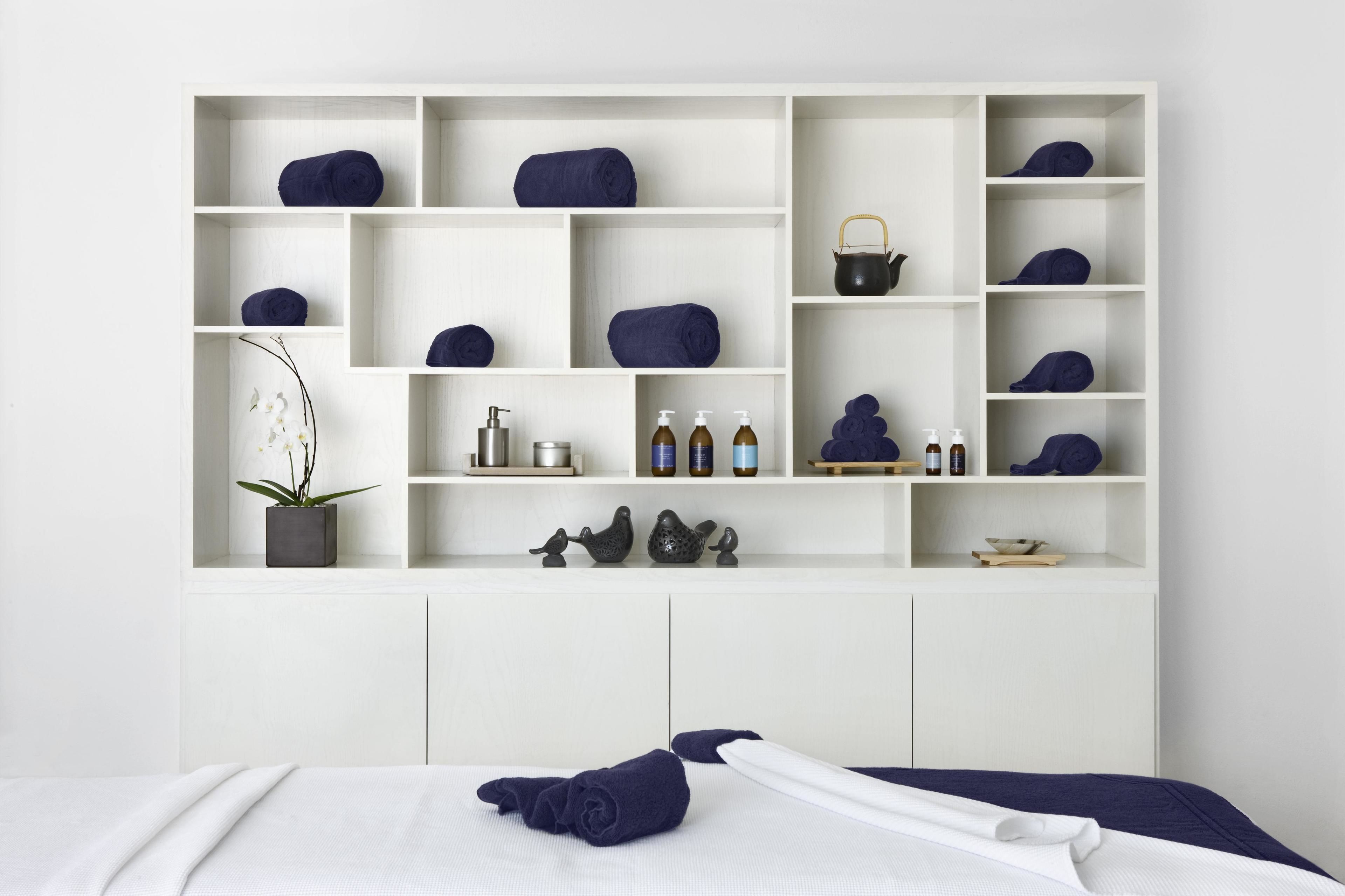 Quarto bem organizado com uma cama, um aparador com toalhas, produtos de higiene e objetos decorativos.