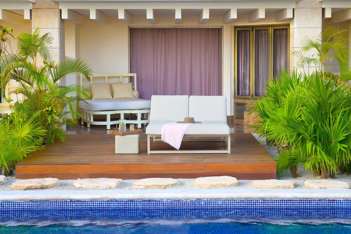 Uma área na piscina com um sofá branco, uma mesa pequena e um vaso de planta.