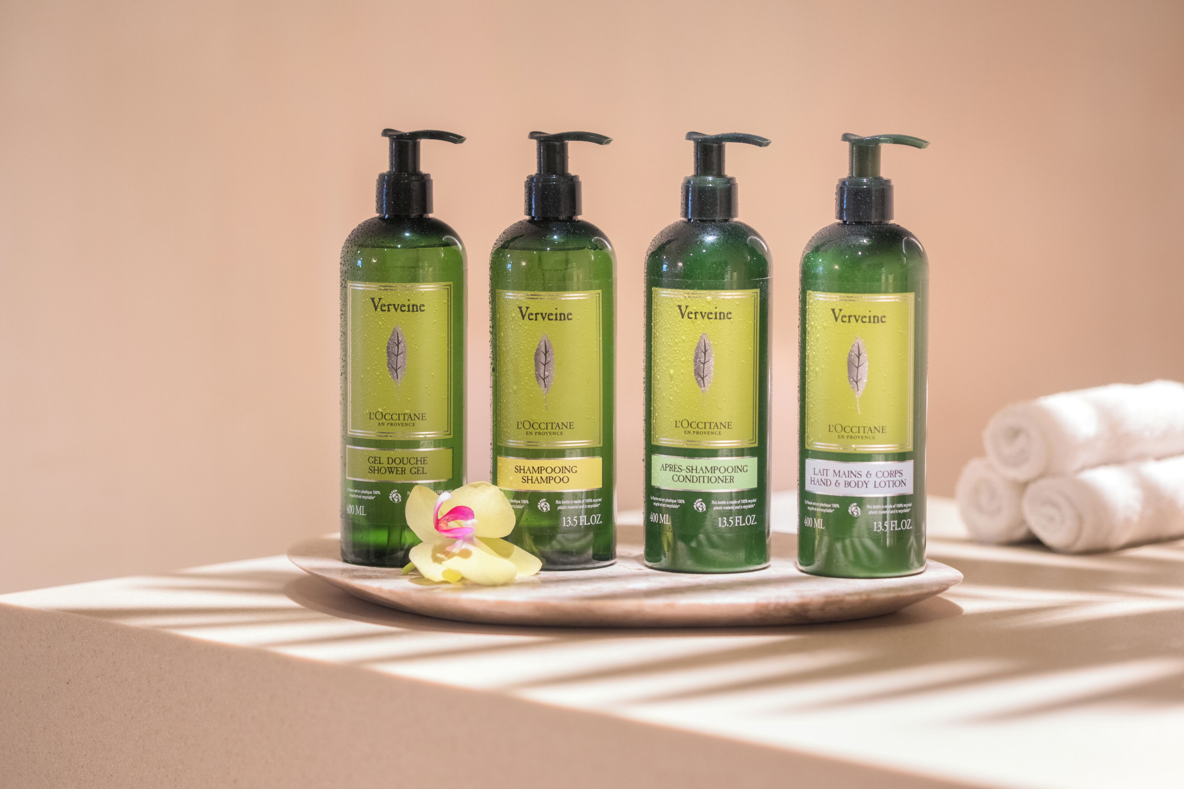 Cuatro botellas de champú y acondicionador L'OCCITANE Verveine sobre una bandeja.