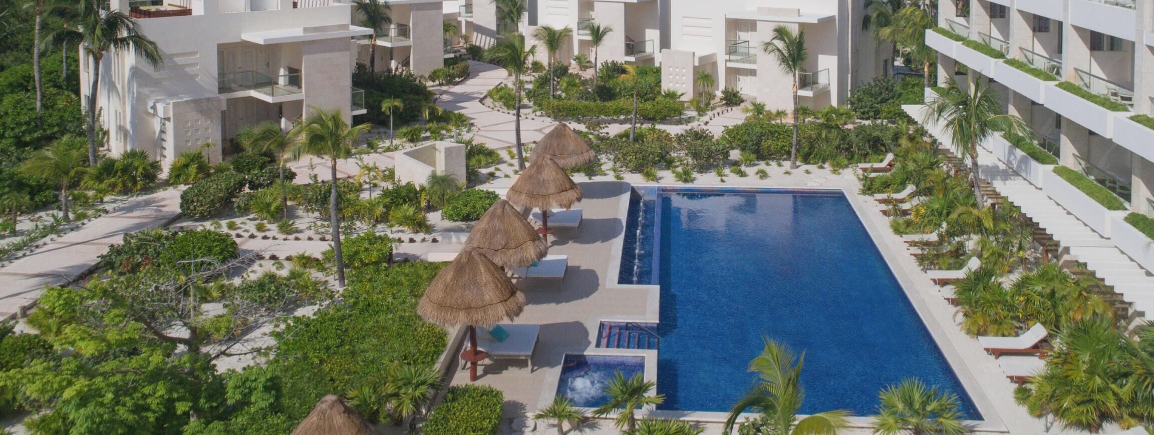 Un resort con una piscina central rodeada de zonas de descanso y palmeras.