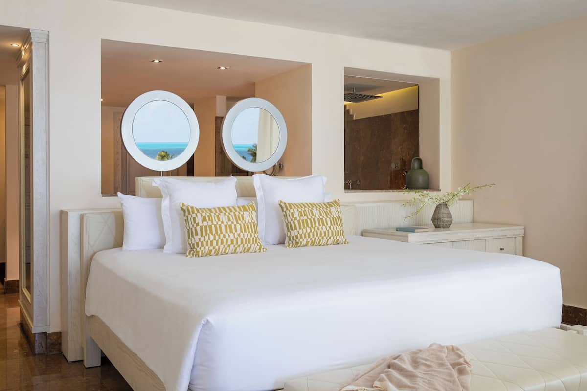 Quarto de hotel com uma cama grande, duas espelhos redondos, uma toucador com um vaso e vista para o oceano.