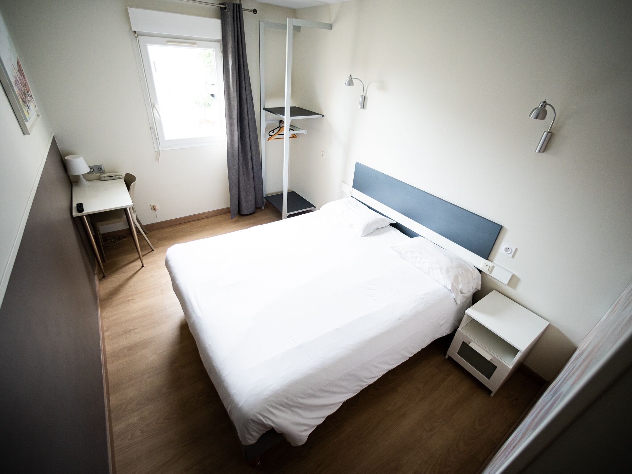 A modern hotel room with a single bed, a desk, and a chair.