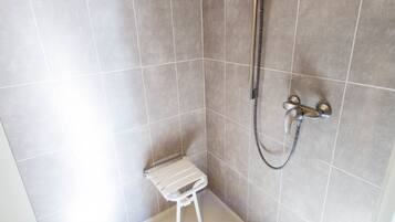 A shower area with a handheld showerhead, a wall-mounted faucet, and a small stool.