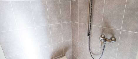 A shower area with a handheld showerhead, a wall-mounted faucet, and a small stool.