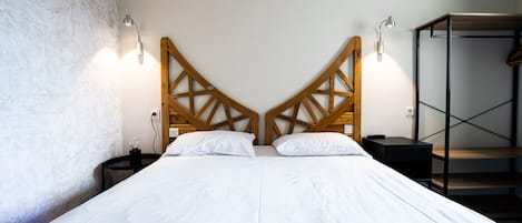 Una cama doble con cabecera de madera, mesitas de noche e iluminación en la pared.