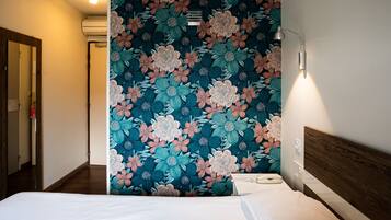 A hotel room with a large floral-patterned wall, a wooden headboard, and a bedside lamp.