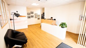 Un área de recepción con un mostrador de madera, un sillón de cuero negro, una lámpara de pie negra y una planta en maceta.