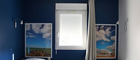 A room with two beds, a window with blinds, and two wall-mounted lamps.