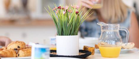 Une table de petit-déjeuner avec des croissants, un pichet de jus d’orange et une petite plante en pot.
