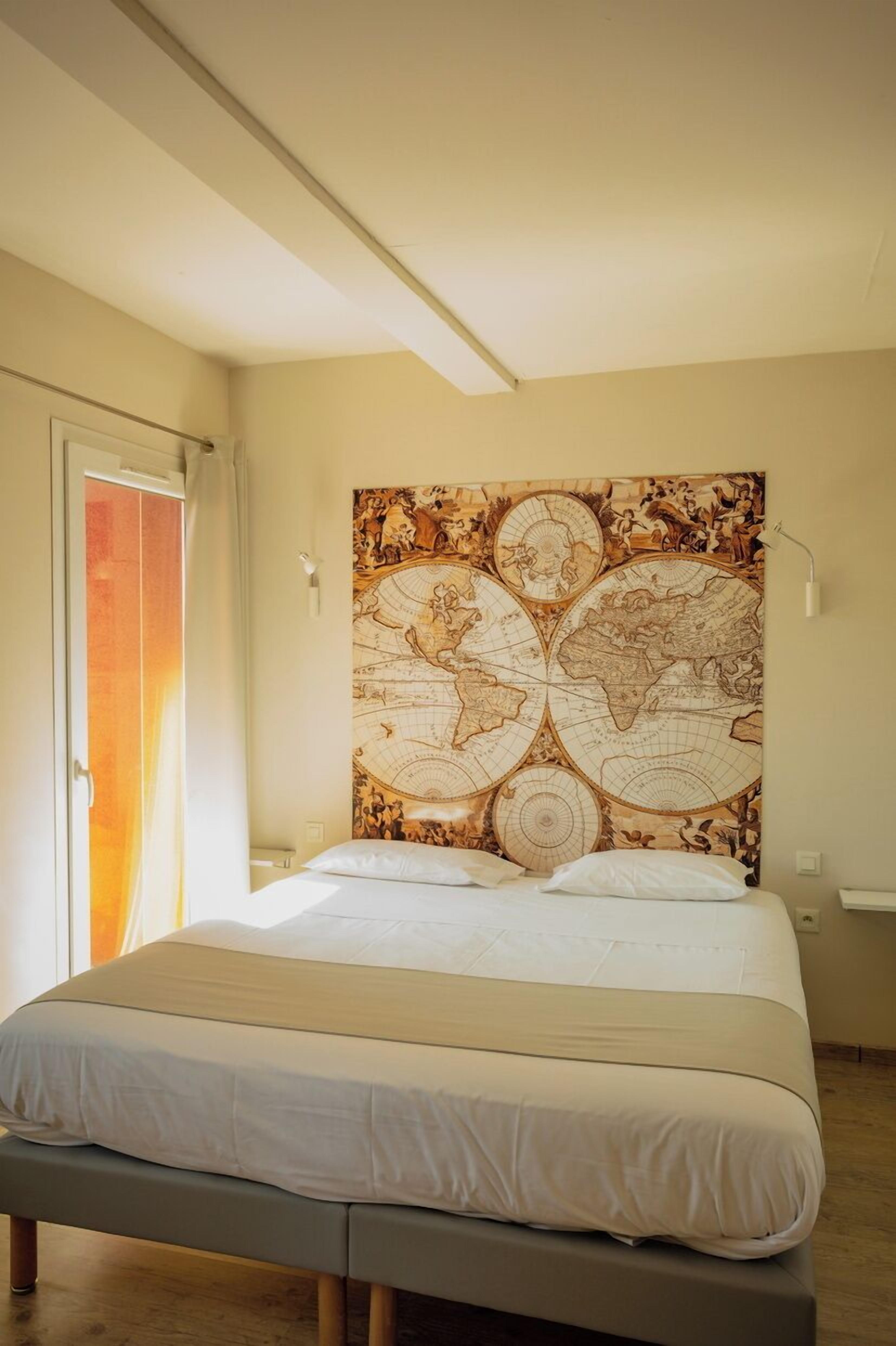 Une chambre avec un grand lit, une tapisserie représentant une carte du monde accrochée au mur, une porte coulissante et une lampe de chevet.
