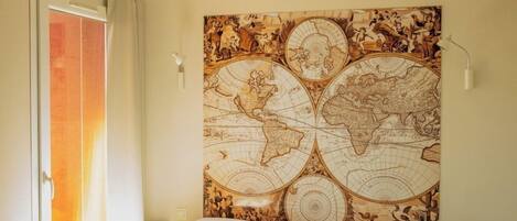 A bedroom with a large bed, a world map tapestry on the wall, a sliding door, and a bedside lamp.
