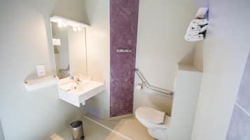 Une salle de bain moderne avec un lavabo blanc, un miroir et des toilettes. On y trouve une poubelle et un porte-serviettes fixés au mur.