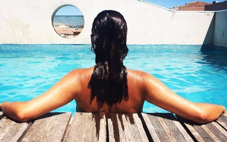 A person relaxing in a pool with a view of the sea through a circular window.