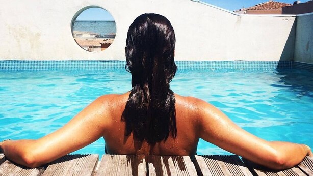 Una persona relajándose en una piscina con vista al mar a través de un ventanal circular.