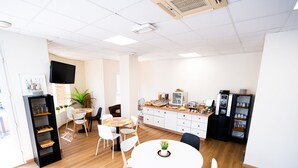 Un comedor moderno con una mesa redonda, sillas blancas y una zona de cocina con electrodomésticos y una cafetera.