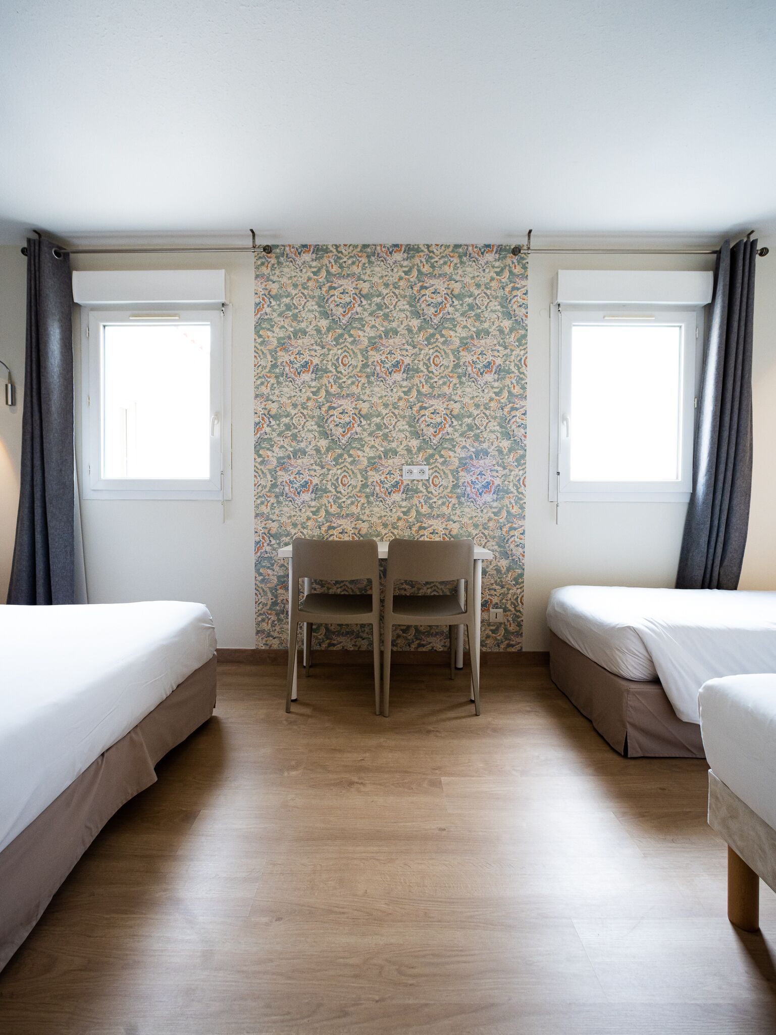 A room with two beds, a table, and a patterned wallpaper.