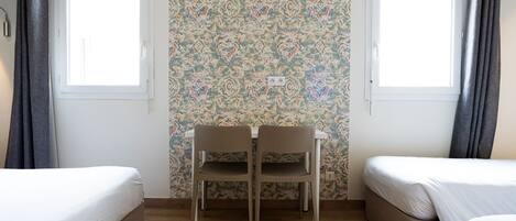 A room with two beds, a table, and a patterned wallpaper.