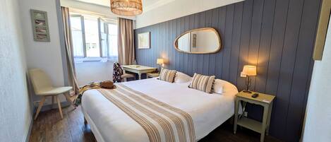 A hotel room with a large bed, two bedside tables with lamps, a chair, a desk, and a large window with curtains.