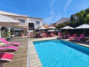 A pool area with wooden deck, pink lounge chairs, and umbrellas. - Logis Hôtel de la Marée - Ile de Ré (Rivedoux-Plage)