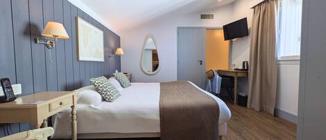 A hotel room with a large bed, bedside lamps, a desk, a chair, a mirror, and a television.