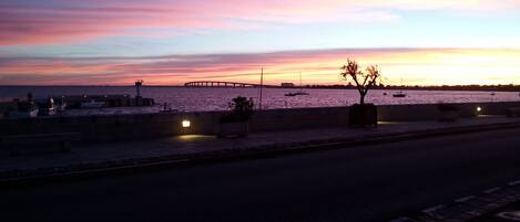 A waterfront scene at dusk with boats docked, a pier, and a tree in the foreground.