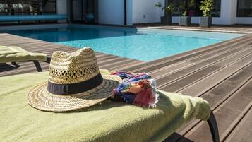 Una tumbona con un sombrero tejido y una bufanda colorida, con vistas a una piscina.
