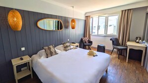 A hotel room with a large bed, a desk, a chair, a mirror, and a window with curtains. - Logis Hôtel de la Marée - Ile de Ré (Rivedoux-Plage)