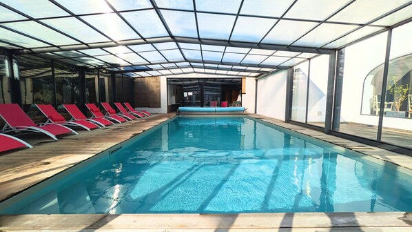 An indoor swimming pool with red lounge chairs and a glass ceiling.