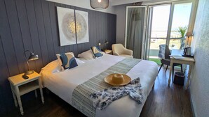 A hotel room with a bed, a desk, a chair, a nightstand, and a large window with a view. - Logis Hôtel de la Marée - Ile de Ré (Rivedoux-Plage)