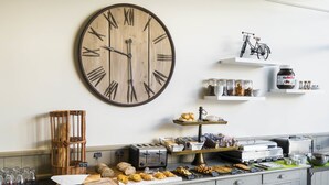 A breakfast buffet with a large wooden clock, wicker baskets, and various food items. - Logis Hôtel de la Marée - Ile de Ré (Rivedoux-Plage)