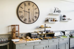 Un buffet de petit-déjeuner avec une grande horloge en bois, des paniers en osier et divers aliments.