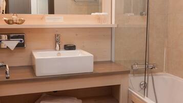 Un baño moderno con un lavabo blanco, cabina de ducha con mampara de cristal y estantes de madera.