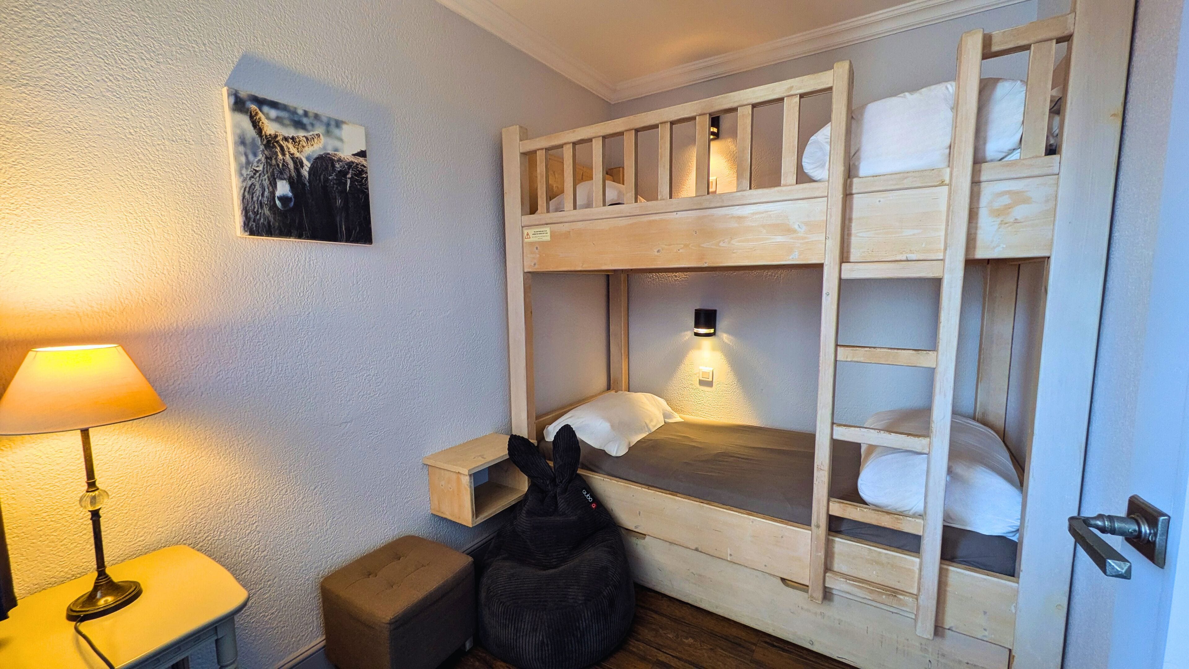 Habitación con literas de madera, una lámpara de noche y un sillón de granos de caucho negro.