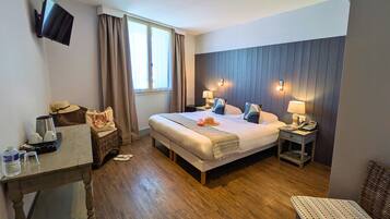 A hotel room with a large bed, bedside lamps, a flat-screen TV, a wooden floor, and a window with curtains.