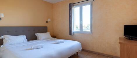 Una habitación de hotel con cama, televisor y ventana con cortinas.