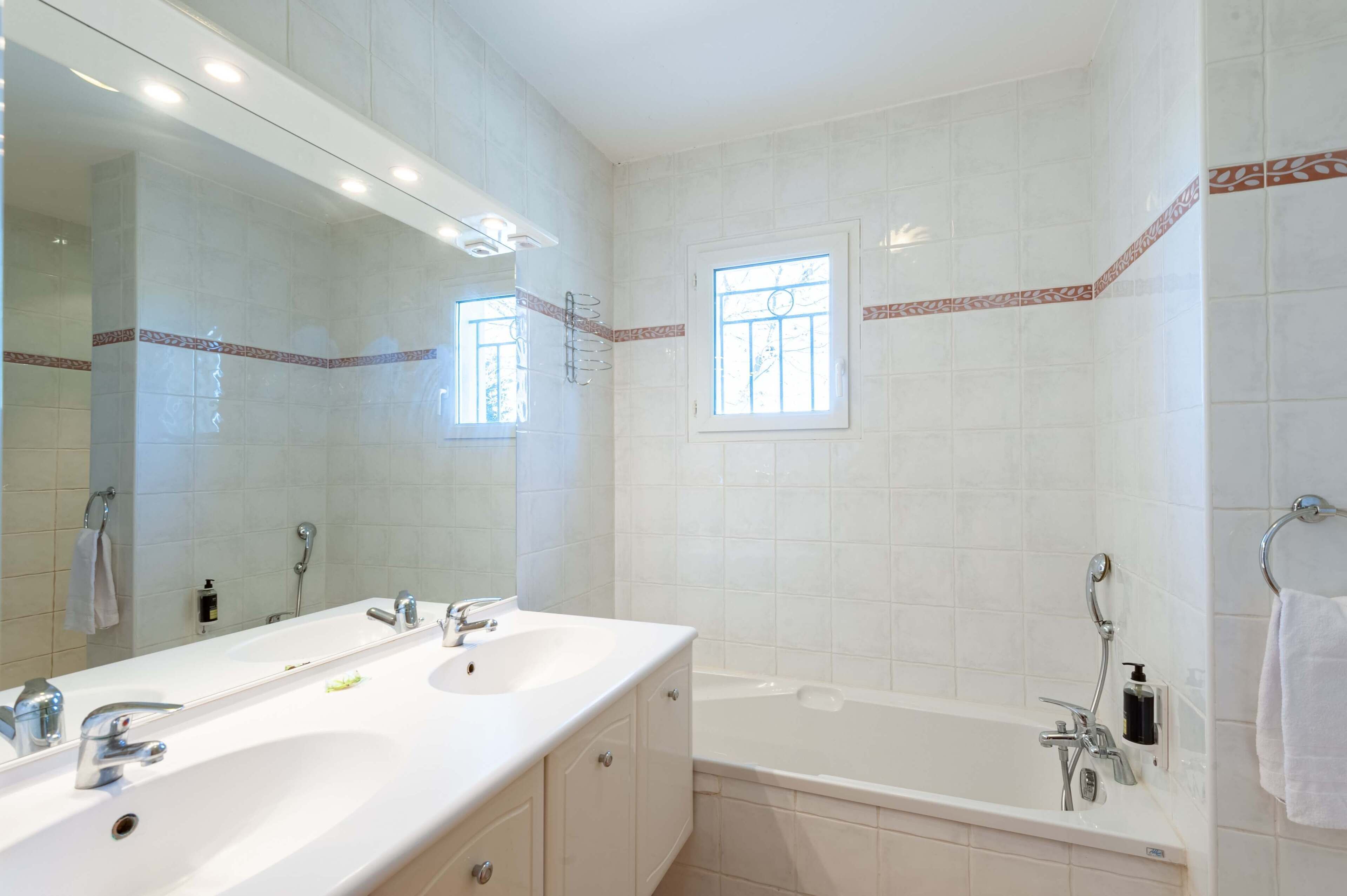 A bathroom with two sinks, a large mirror, a bathtub, and a window.