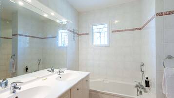 A bathroom with two sinks, a large mirror, a bathtub, and a window.