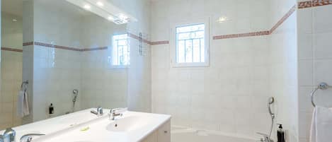A bathroom with two sinks, a large mirror, a bathtub, and a window.