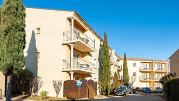 Un immeuble résidentiel à plusieurs étages, doté de balcons, d’une entrée sécurisée et de voitures garées.