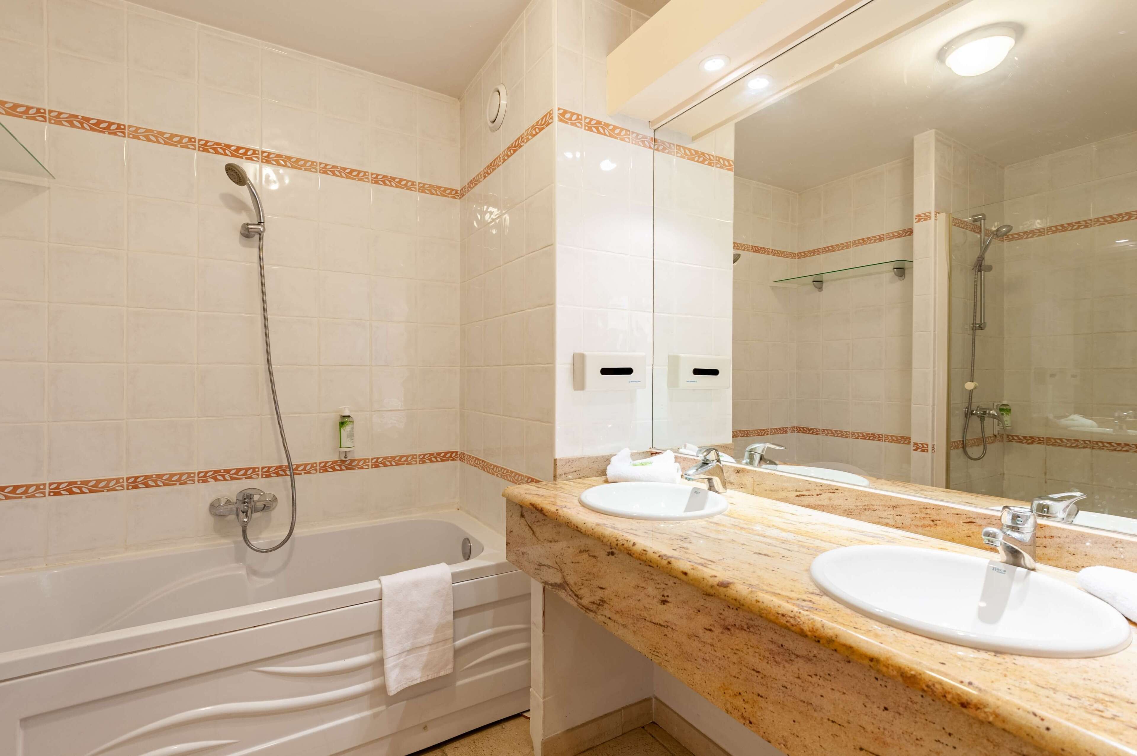 Une salle de bain avec une baignoire, deux lavabos, un grand miroir et un espace douche.