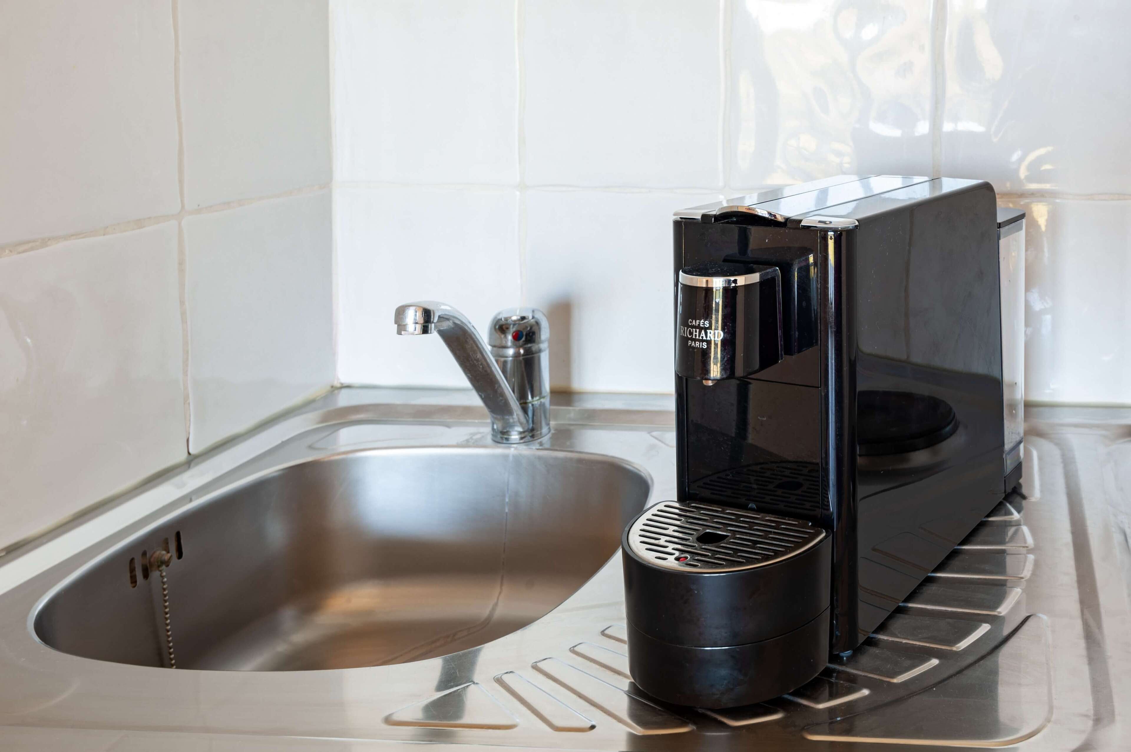 Une cuisine moderne dotée d’un évier en acier inoxydable, d’une machine à café noire et d’un récipient noir.