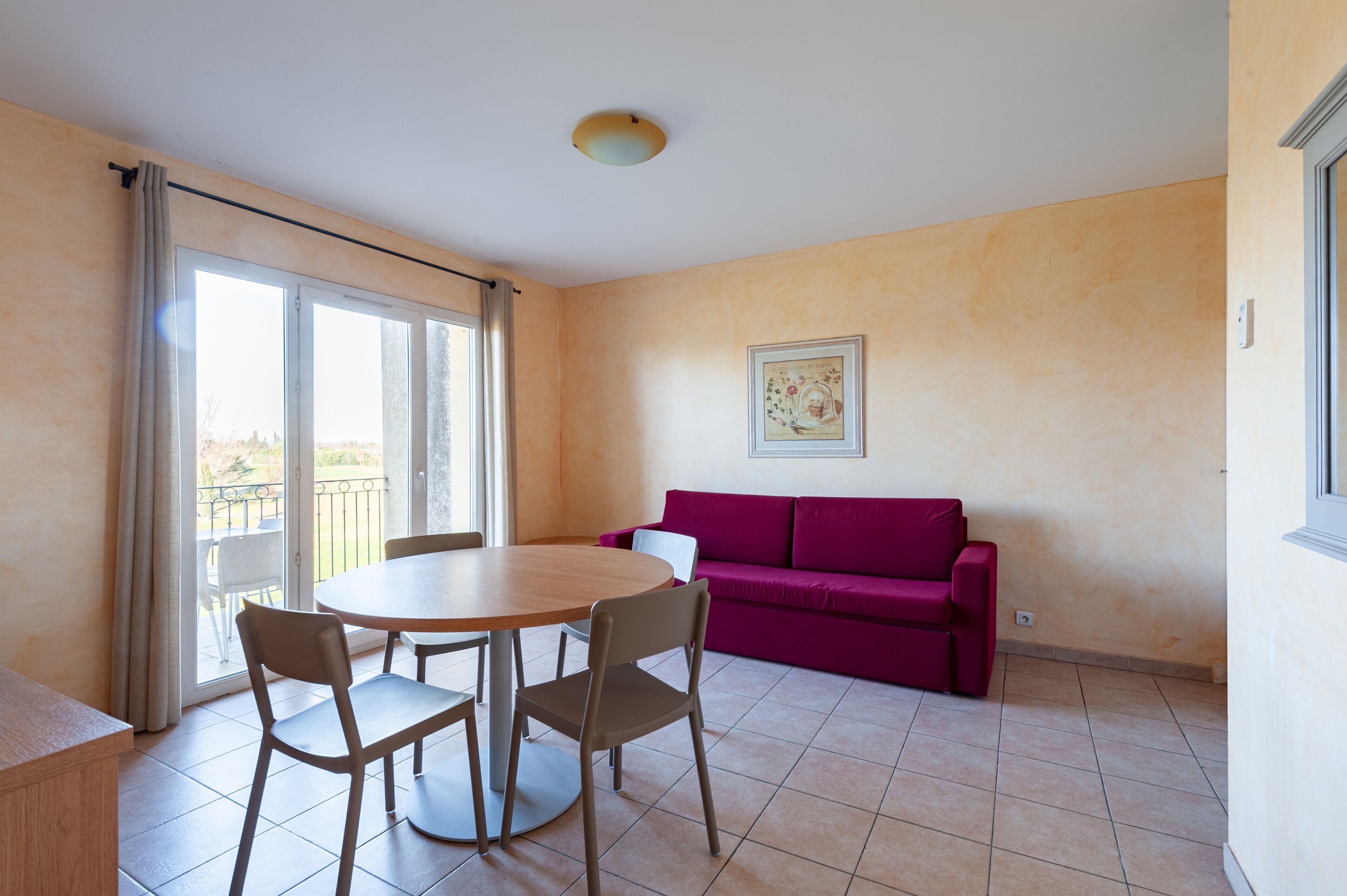 A room with a round table and chairs, a purple sofa, and a large window with curtains.