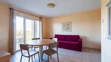 Une pièce avec une table ronde et des chaises, un canapé violet et une grande fenêtre avec des rideaux.