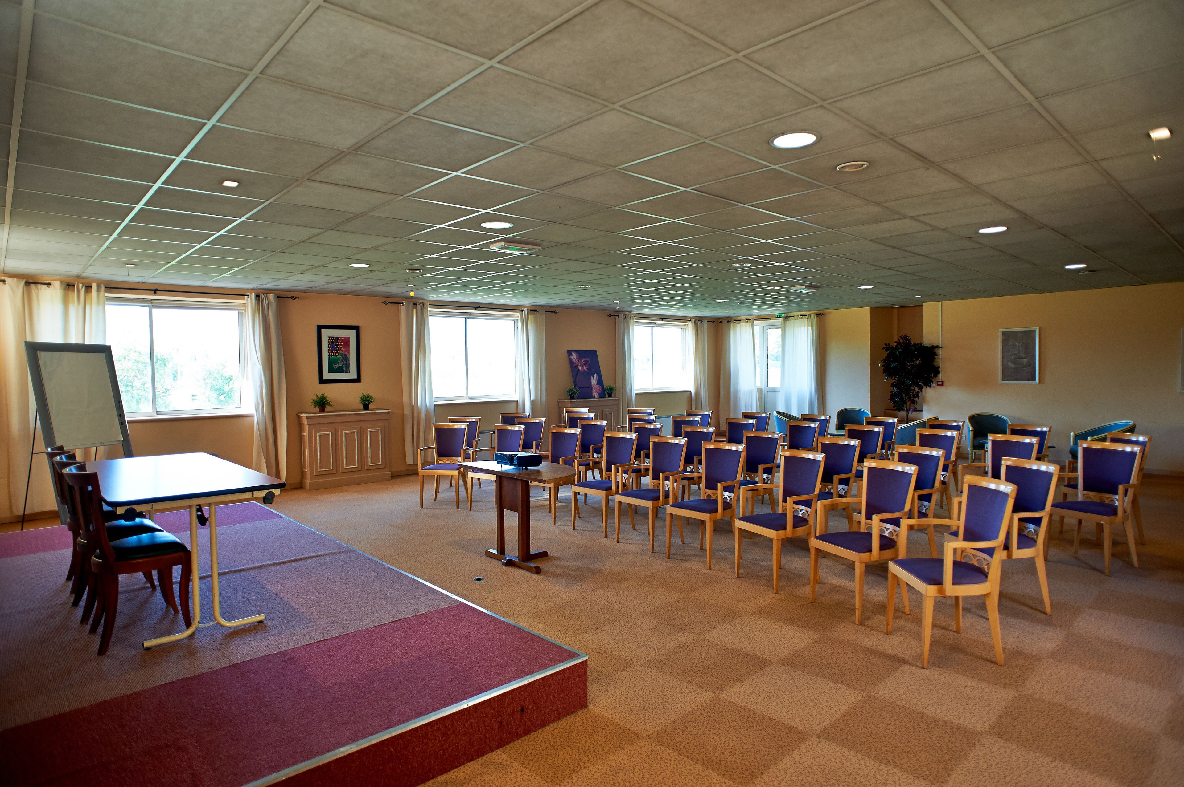 A conference room with a large table, multiple chairs, a whiteboard, and windows with curtains.