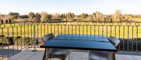 A balcony with a table and chairs overlooking a well-maintained lawn and trees.
