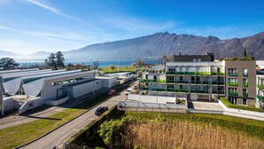 A modern building with a flat roof and a large glass facade, surrounded by a well-maintained lawn and a road with cars. - ResidHotel Azuréa (Aix-les-Bains)