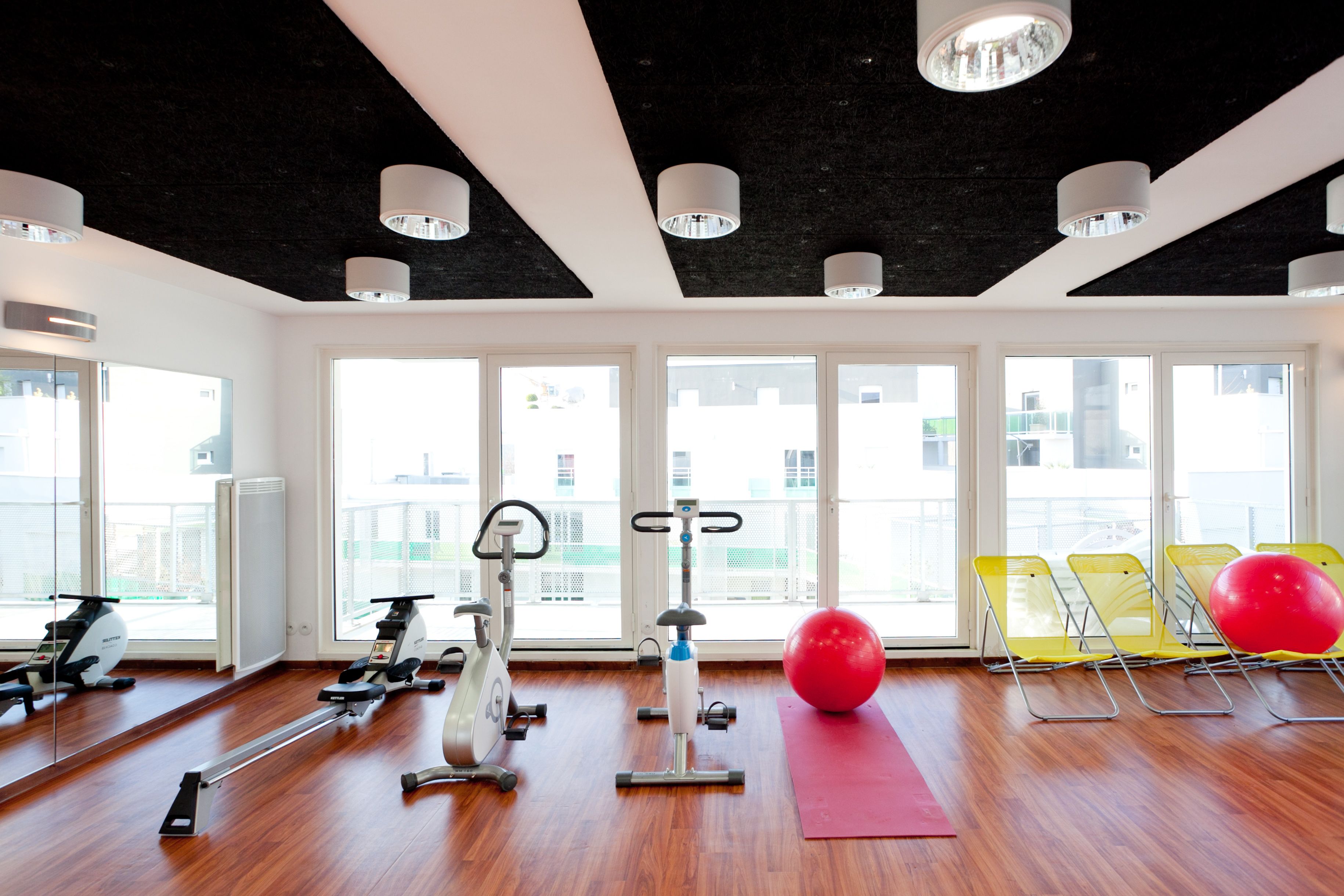Ein Fitnessraum mit Trainingsgeräten, großen Fenstern und einem roten Trainingsball.