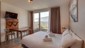 A hotel room with a bed, a desk, a TV, and a view of the outdoors. - ResidHotel Azuréa (Aix-les-Bains)